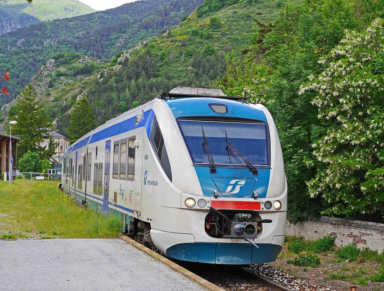 Treno panoramico in movimento attraverso paesaggi mozzafiato italiani, con montagne e valli verdi.